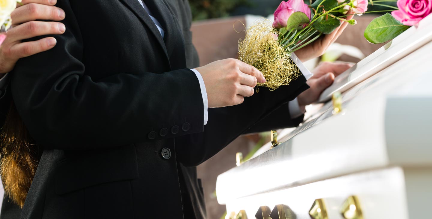 Trauernder legt Hand und Blumen auf einen Sarg mit goldenen Verzierungen