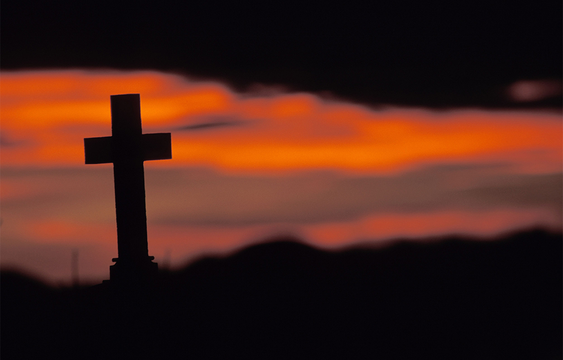 Sonnenuntergang vor Grabsteinkreuz auf einem Friedhof