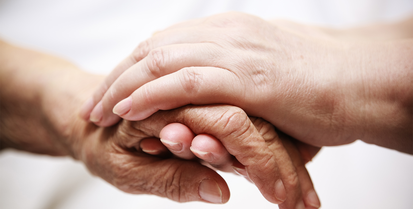 Erwachsener hält die Hand eines älteren Menschen