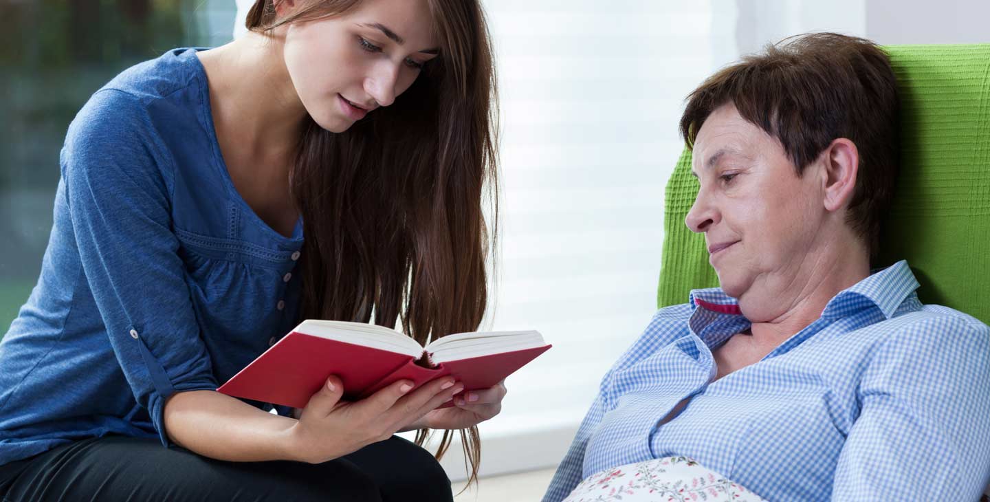 junge Frau liest älterer Frau aus einem Buch vor