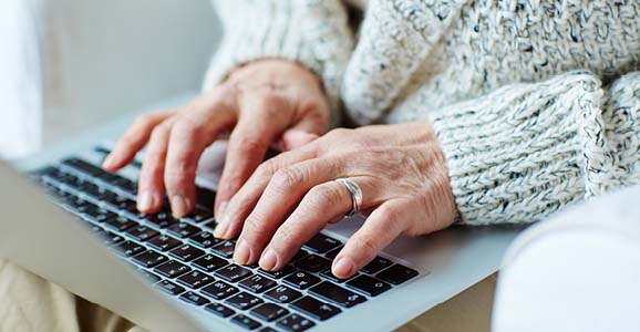 Hände einer Seniorin tippt auf dem Laptop