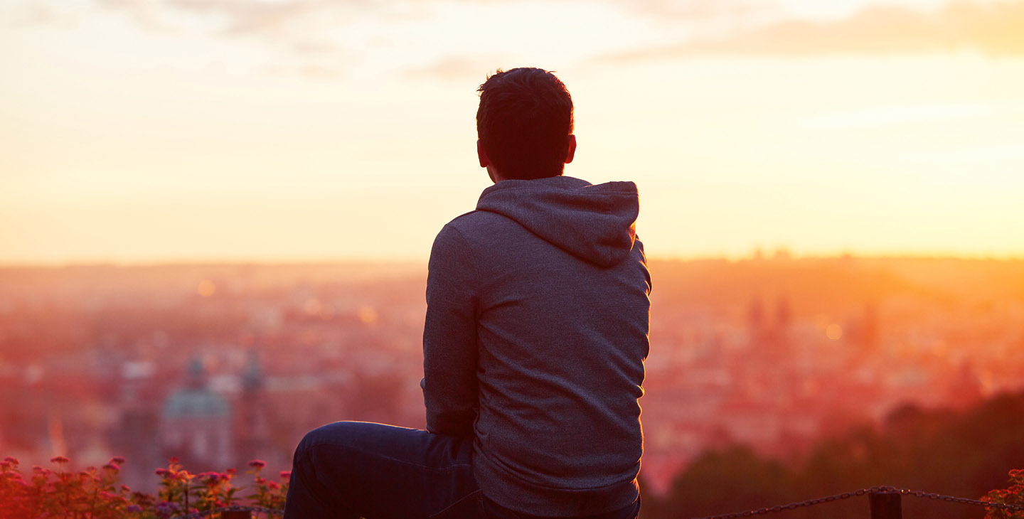 Mann in Kapuzenpulli schaut in den Sonnenuntergang