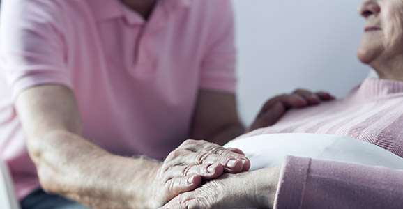 älterer Mann hält die Hand seiner Frau auf dem Bett