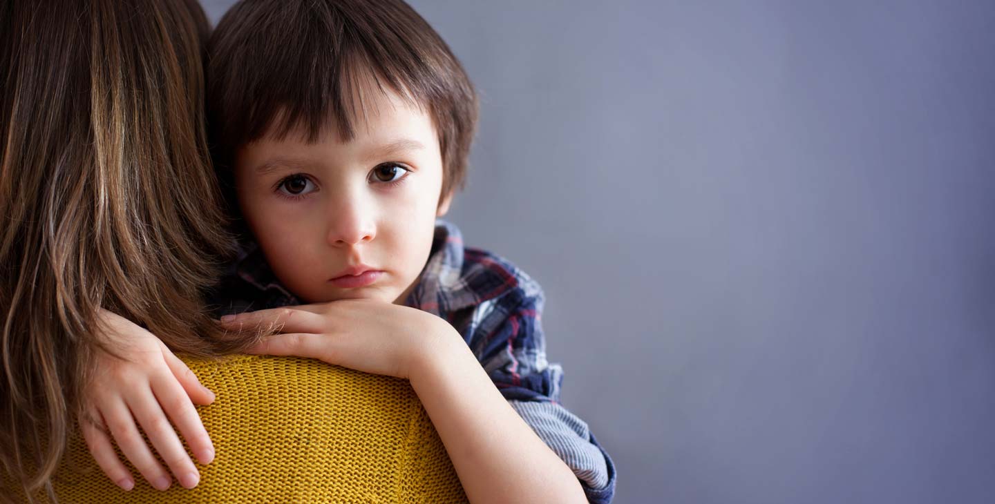 Junge schaut traurig uns ist auf den Armen seiner Mutter