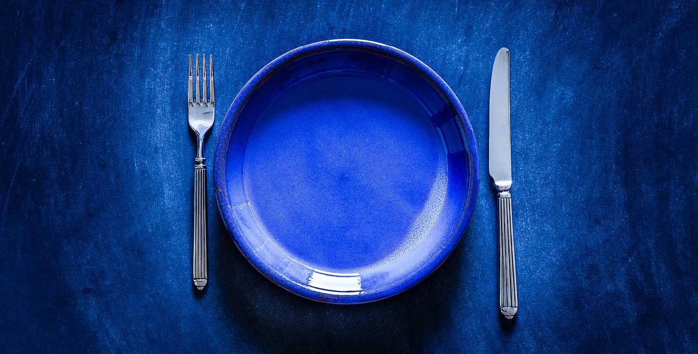Blauer Teller mit Gabel und Messer auf einem blauen Hintergrund