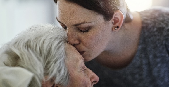 Tochter küsst ältere kranke Mutter auf die Stirn