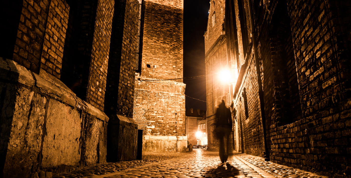 Person spaziert, durch eine beleuchtete Altstadt, in der Nacht