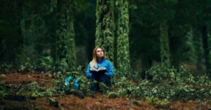 Lifestyle-Aufnahme einer jungen Frau im Wald, die sitzt und ein Buch liest
