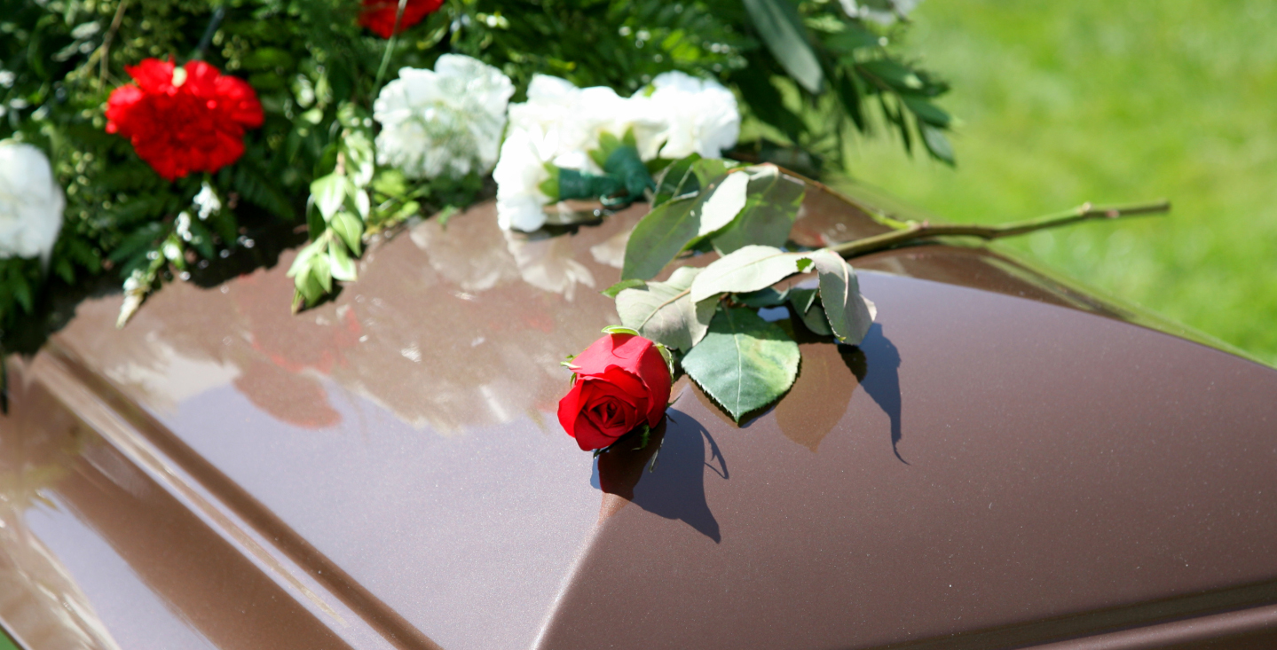 brauner Sarg mit einer Rose und Blumenschmuck
