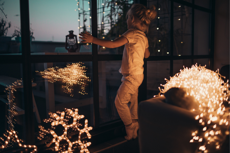 Lichterketten: Kind schaut in der Dämmerung aus dem Fenster