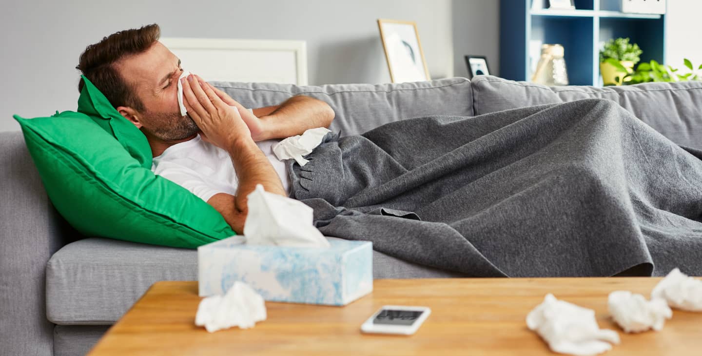 Männer mit Schnupfen oder Männergrippe liegt schneuzend auf dem Sofa
