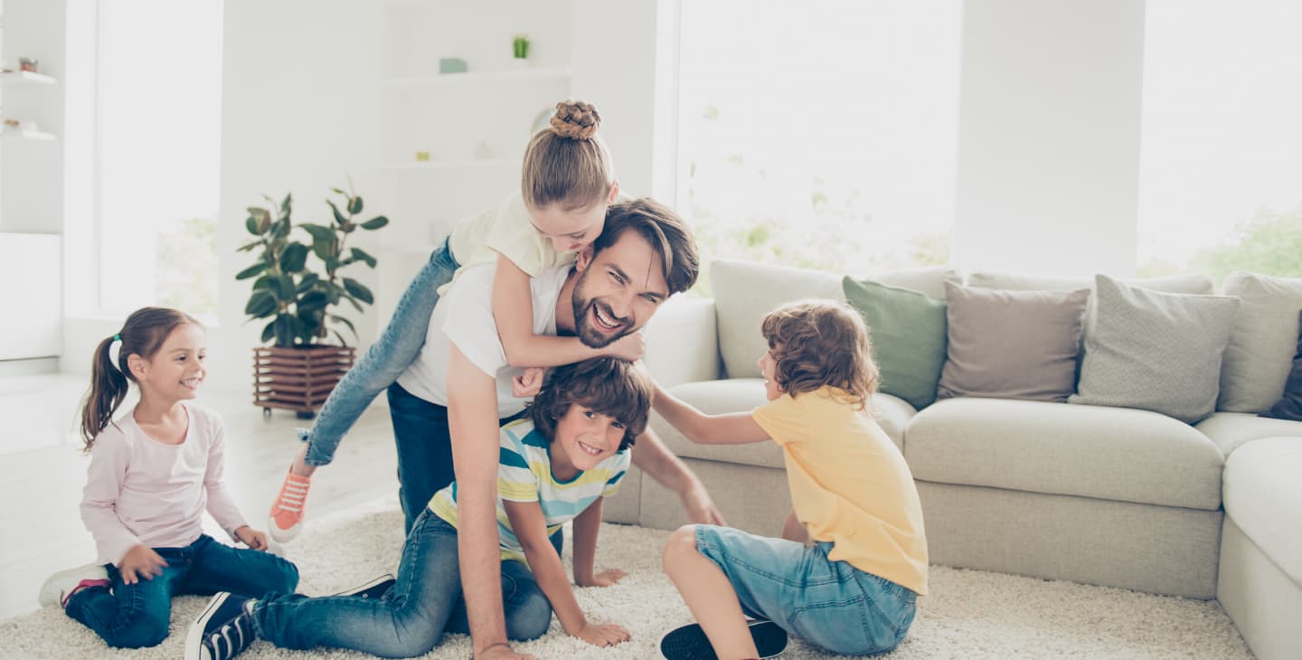 Papa spielt mit vier Kindern im Wohnzimmer