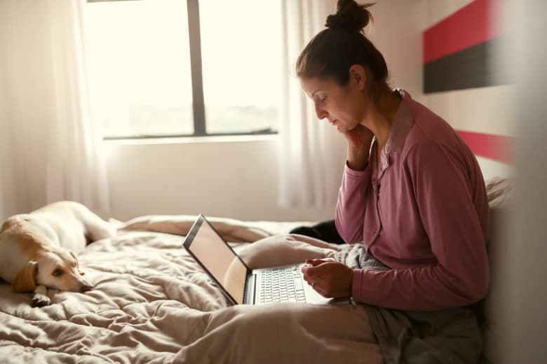 Frau sitzt besorgt im Bett mit dem Laptop auf dem Schoss