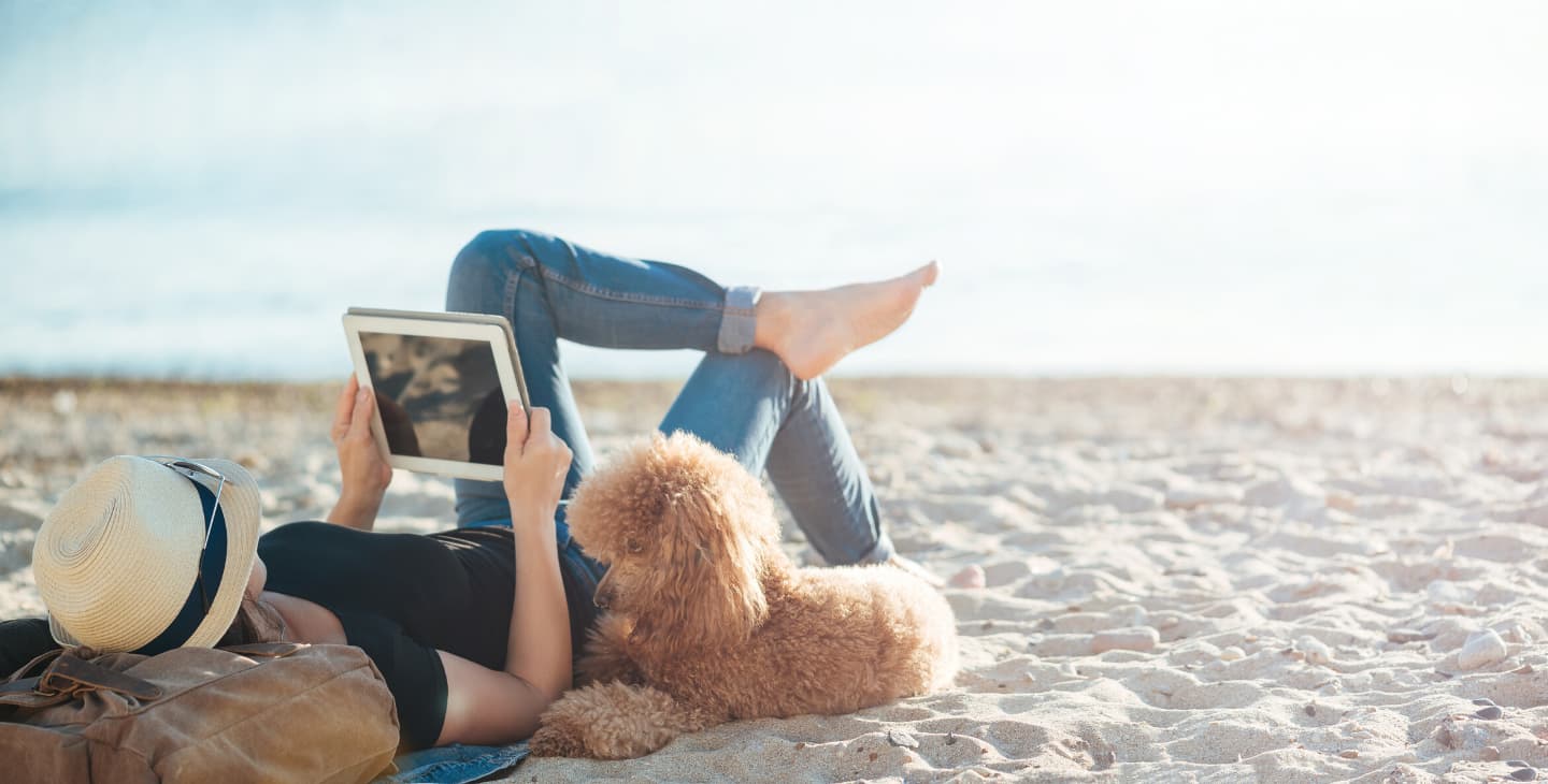 Frau liegt am Sandtrand und liest auf Tablet