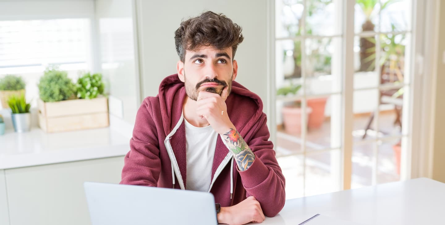 tätowierter Mann überlegt am Laptop