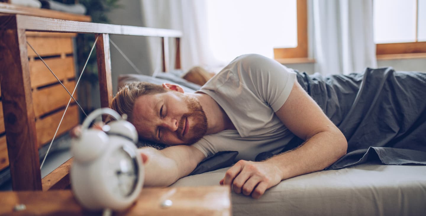 Mann liegt im Bett und wacht langsam auf