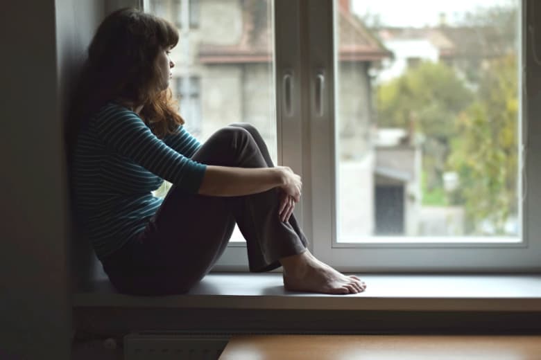Frau sitzt einsam auf Fensterbrett