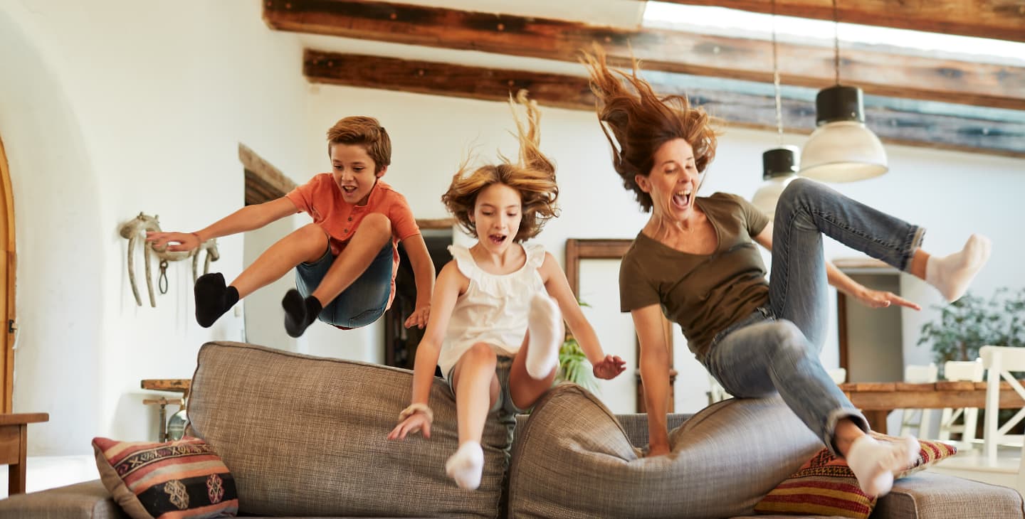 Frau springt mit zwei kleinen Kindern auf ein Sofa