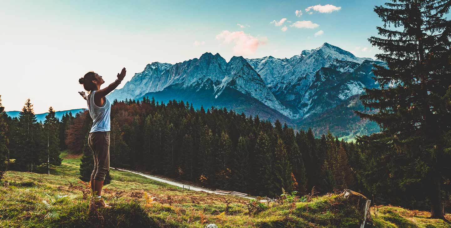 Frau steht vor Bergmassiv und breitet die Arme aus