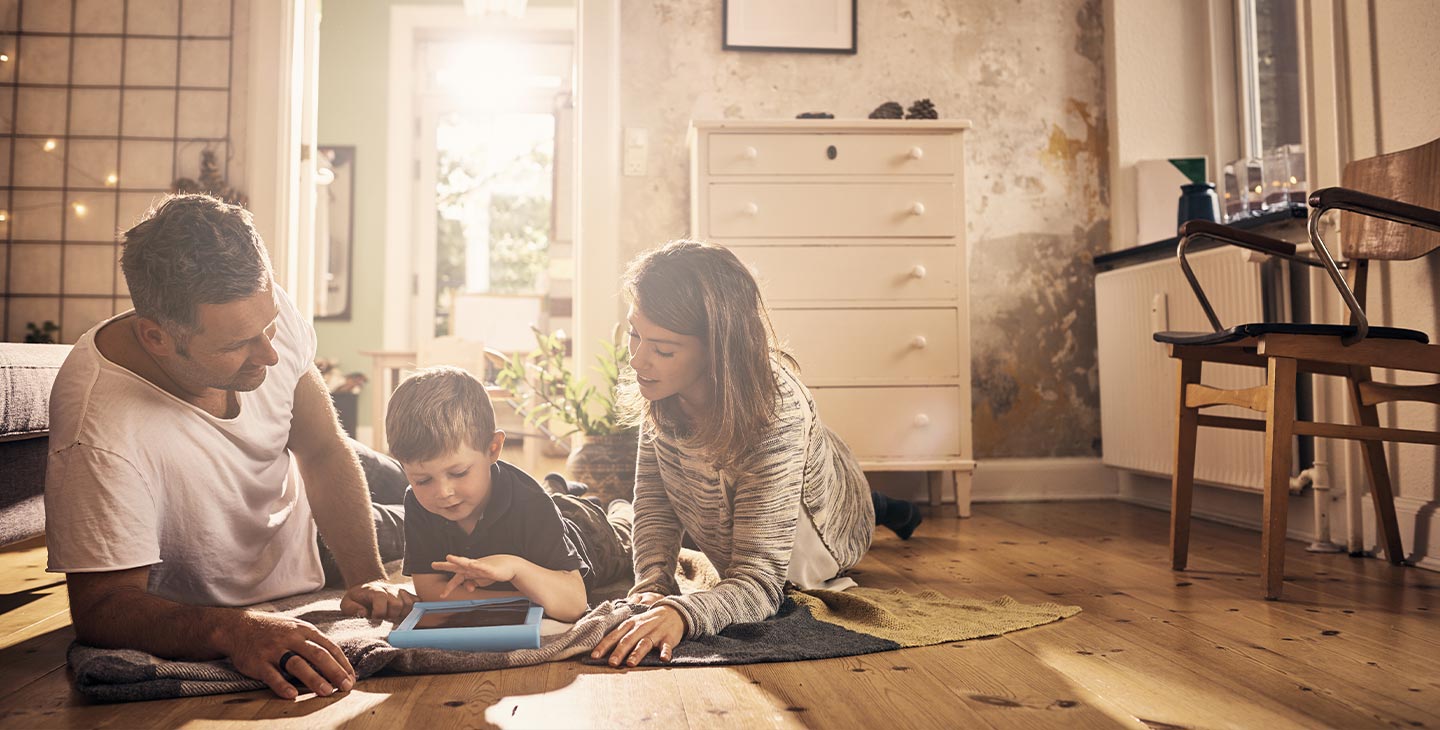 Familie mit kleinem Kind spielt im Wohnzimmer auf einem Tablet