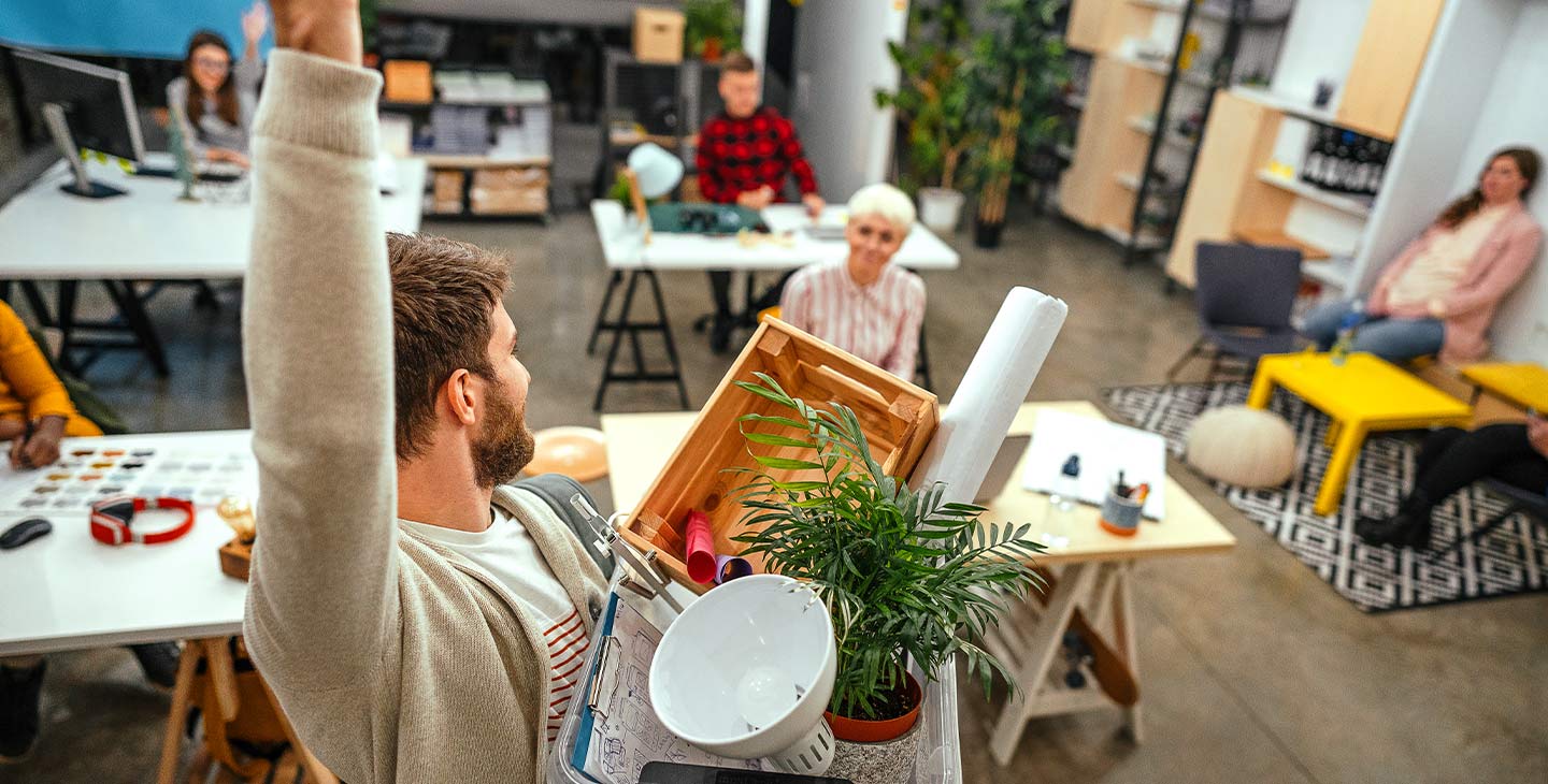 Mitarbeiter verlässt seinen Arbeitsplatz und winkt fröhlich den anderen zu