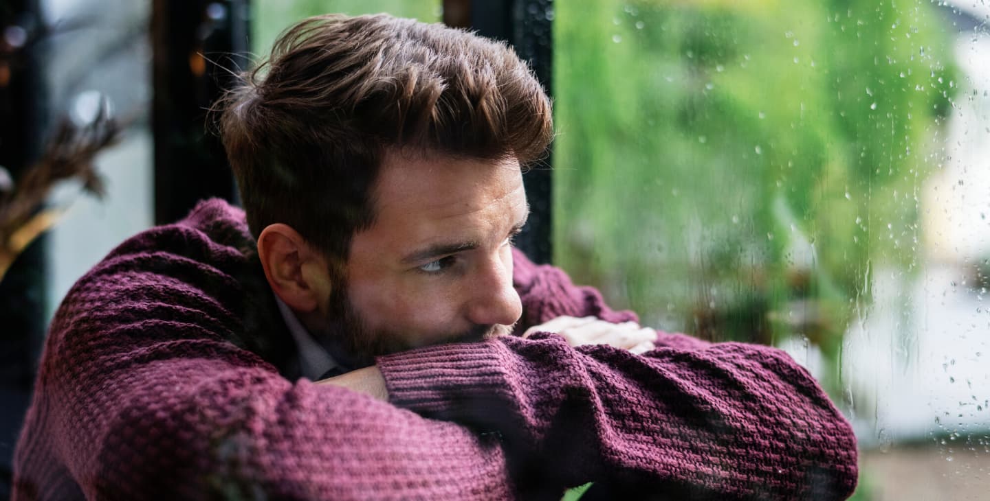 nachdenklicher Mann schaut bei Regen aus dem Fenster