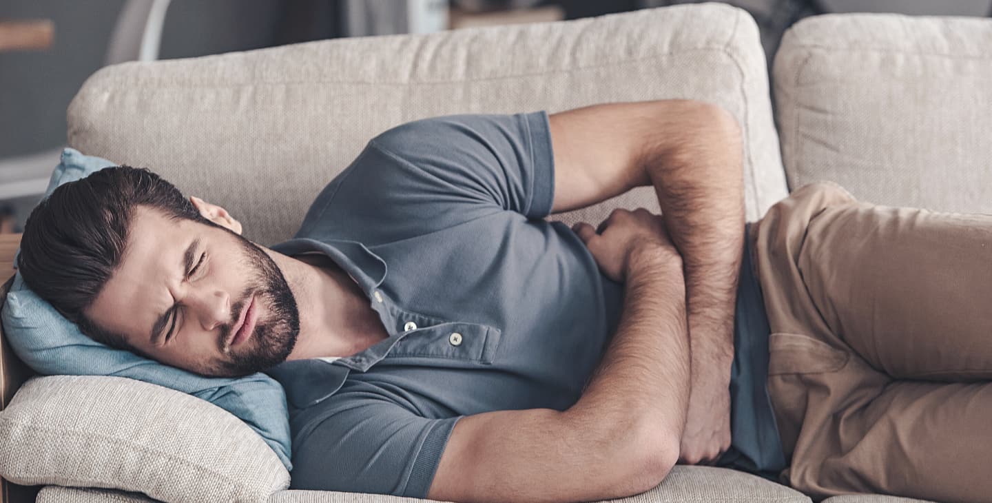 Mann liegt mit Bauchschmerzen auf dem Sofa