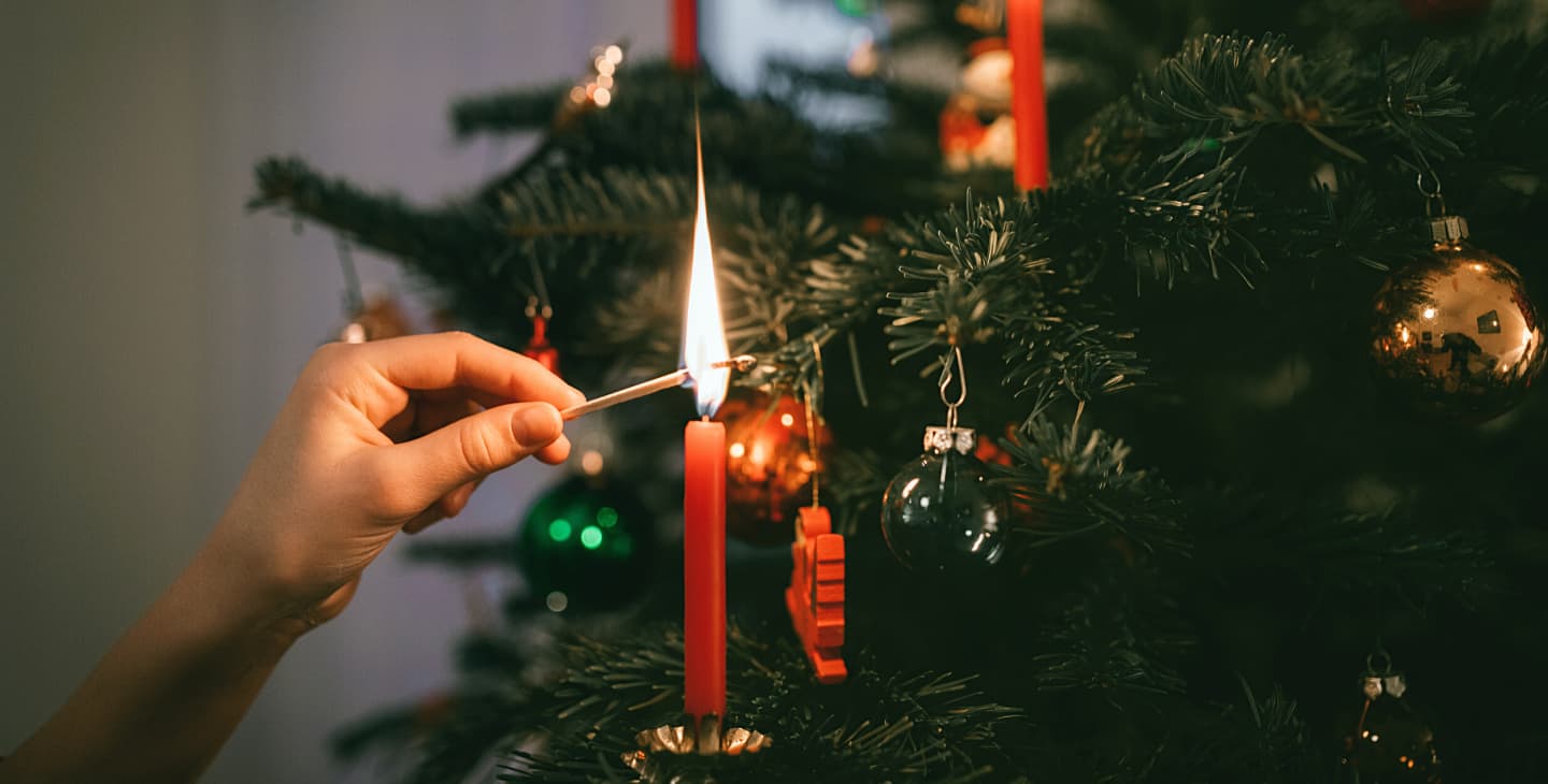 Frauenhand zündet rote Kerze an einem Weihnachtsbaum an