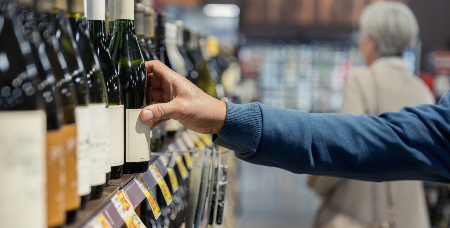 Mann nimmt Weinflasche aus Supermarktregal