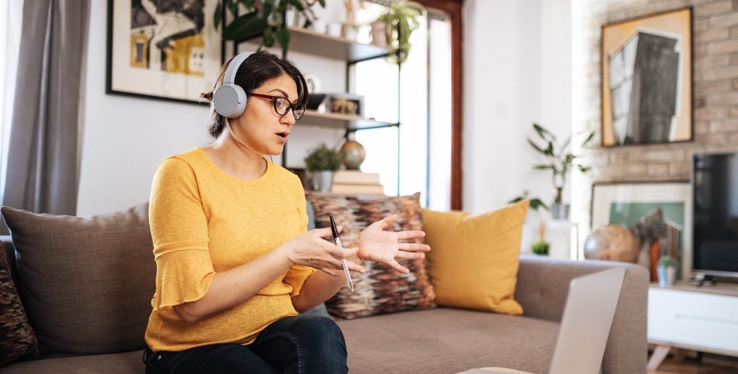 Frau mit Headset auf Couch vor Laptop