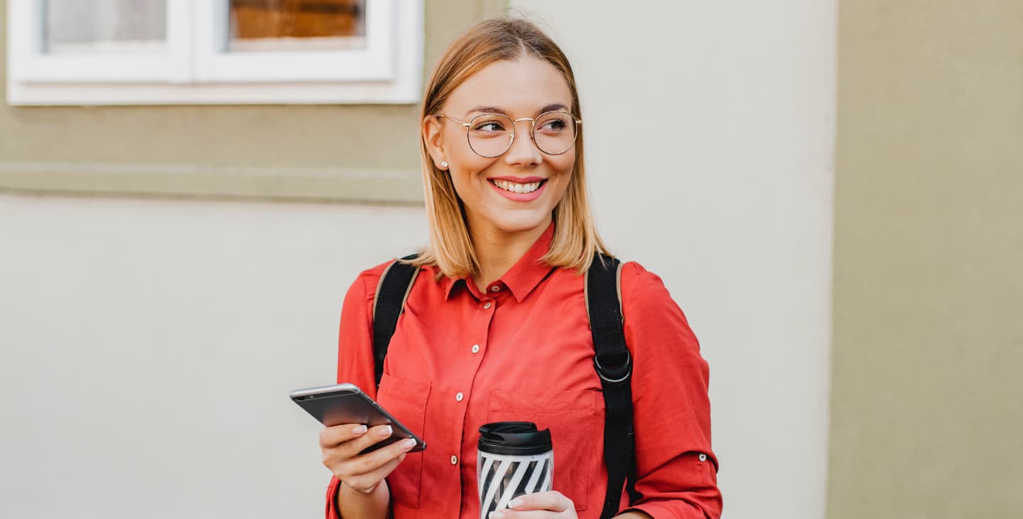 junge Frau mit rotem Hemd hält ihr Smartphone in der Hand