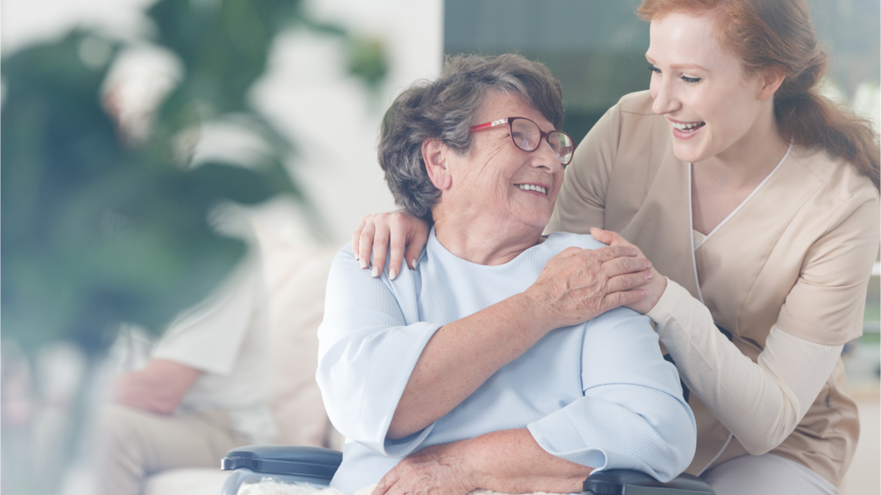 Seniorin in Rollstuhl mit fröhlicher Pflegerin