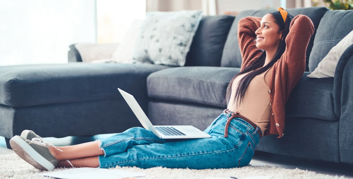 Frau sitzt im Wohnzimmer auf dem Boden mit Laptop auf dem Schoß