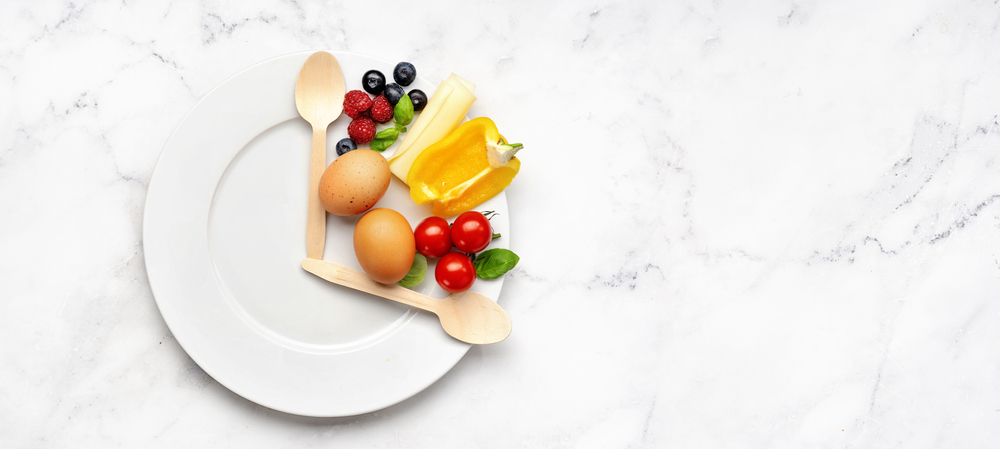 Teller mit zwei Holzlöffeln zwei Eiern und Obst und Gemüse