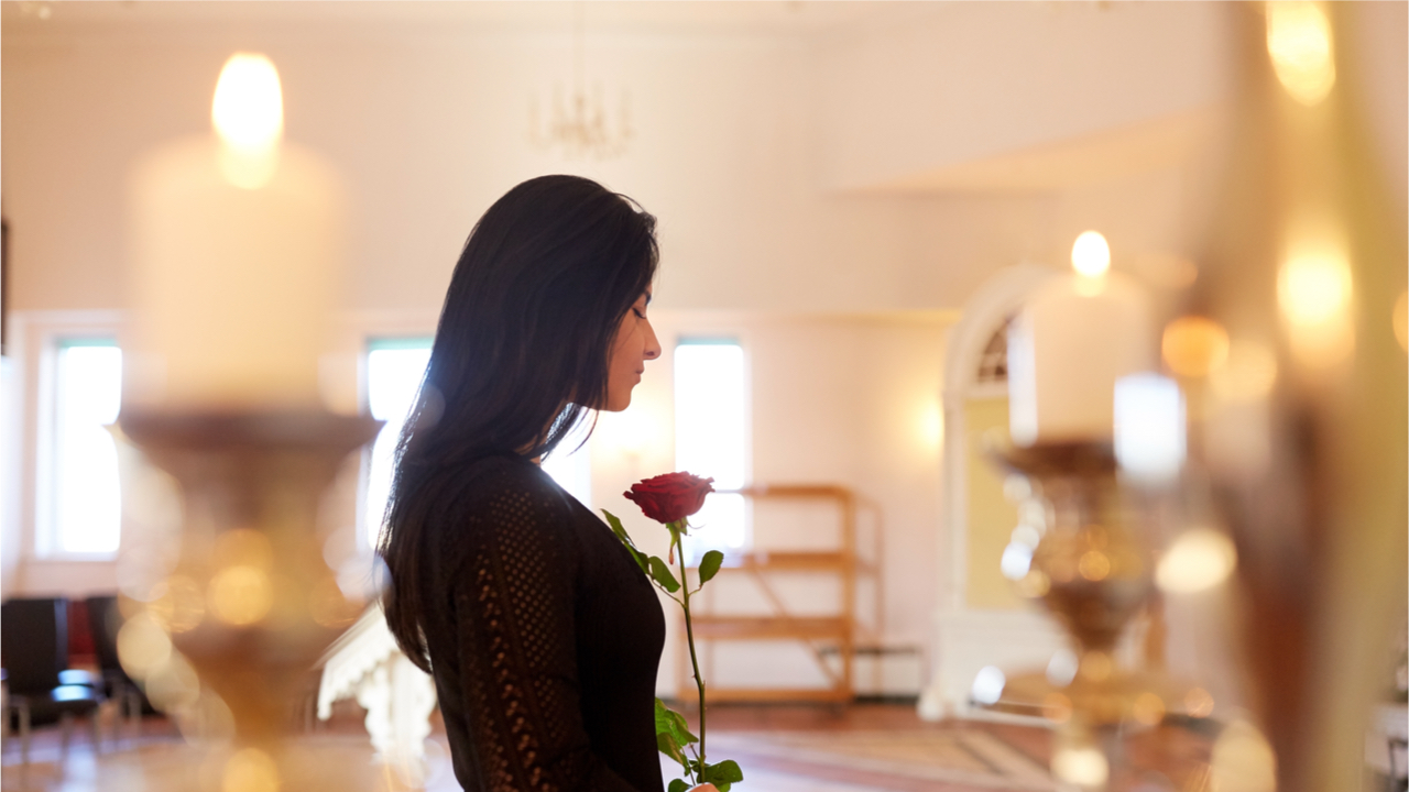 Frau mit schwarzen Haaren trauert und hält eine Rose in der Hand
