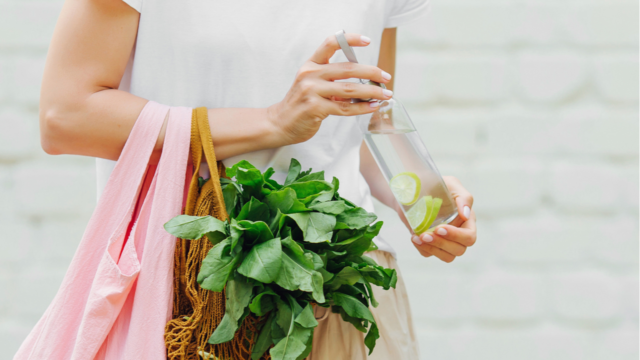 Frau mit Salat in Einkaufstasche und Trinkflasche mit Wasser und Zitrone