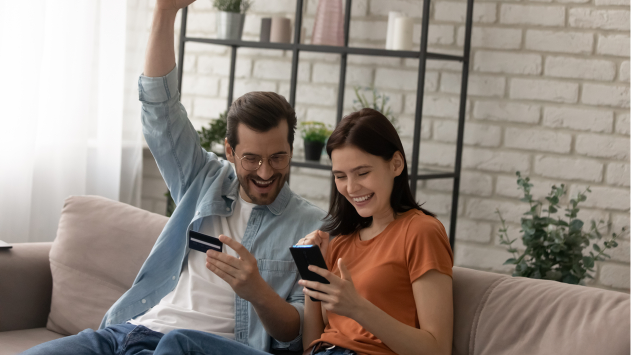 Pärchen auf Sofa yubelt mit Kreditkarte in der Hand