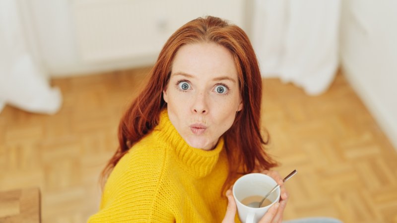 Frau schaut erstaunt und hält eine Tasse Kaffee in der Hand