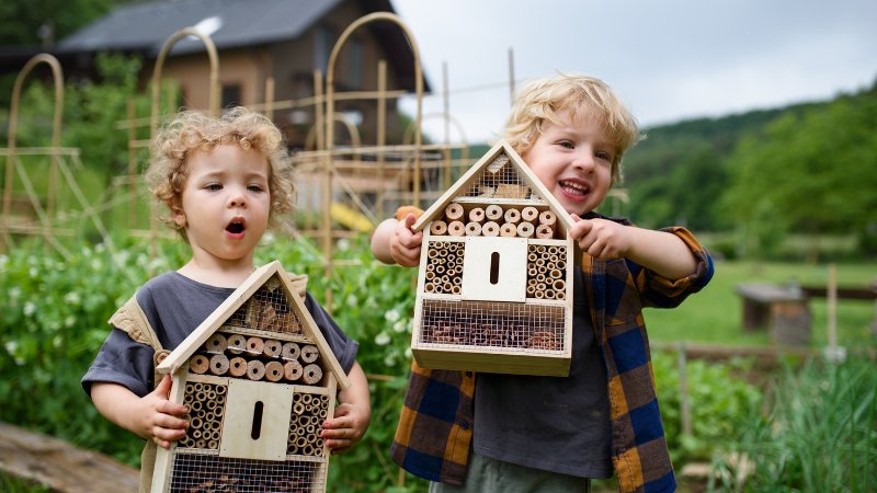 Ein kleines Mädchen und ein kleiner Junge halten stolz ein Insektenhotel in den Händen