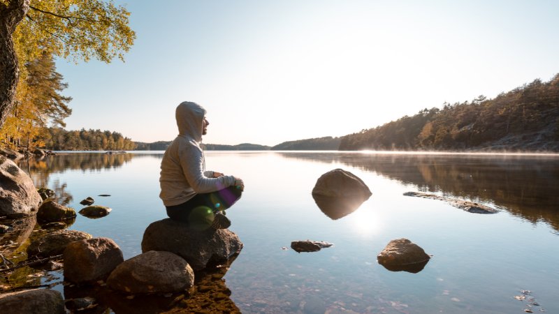 Mann sitzt auf einem Stein und blickt auf den See
