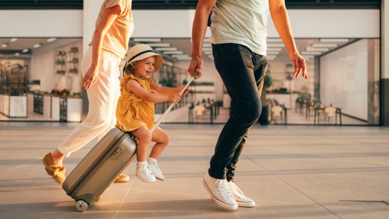 Familie reist mit kleinem Kind. Kind sitzt auf Trolley