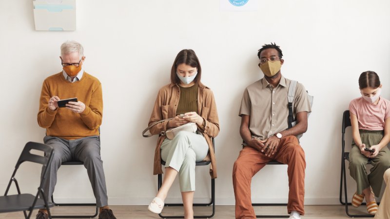 Wartezimmer mit Patienten und Mundschutz