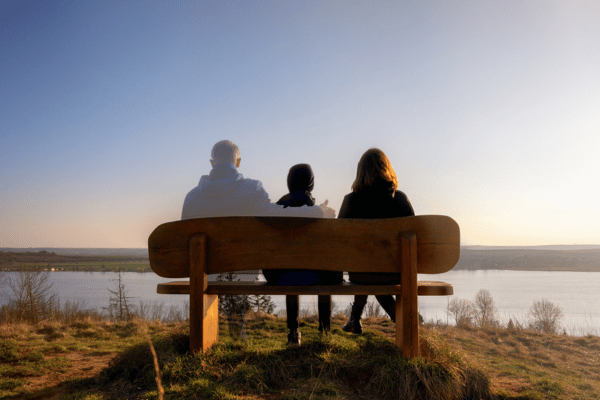 Familie sitzt auf einer Bank mit Seeblick