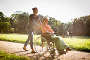 Junge Frau schiebt Seniorin im Rollstuhl durch Park